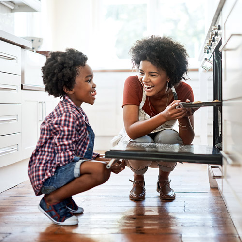 women knelt down speaking to her son whilst cooking and placing food into the oven