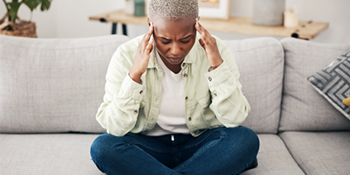 woman sitting on grey sofa with fingers placed on temples