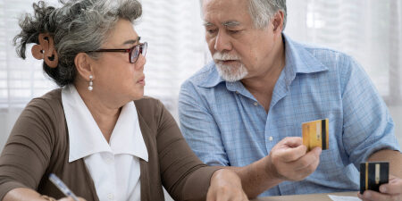 How-to-pay-off-credit-card-debt-feature woman and man sitting at table. man holding credit card, woman writing on piece of paper
