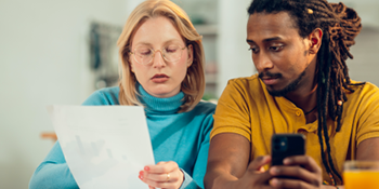 male and female sitting next to each other, female holding piece of paper which both are looking at