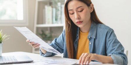 woman holding piece of paper and tapping on calculator