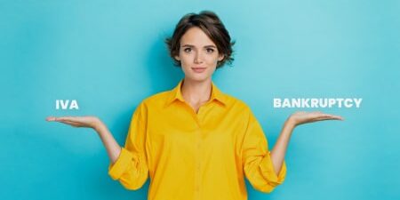 Whats-the-differnce-between-iVA-and-bankruptcy_-feature woman wearing yellow jumper holding out hands either side of her like scale. Text on one hand reads IVA, text on other hand reads Bankruptcy.