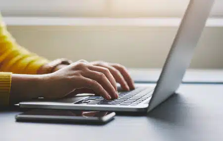 Women with a yellow jumper typing on a laptop