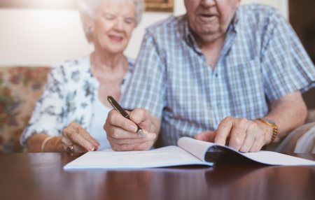 An elderly couple writing in a booklet