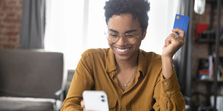 Woman holding a blue credit card smiling at her mobile