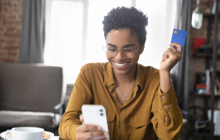 Woman holding a blue credit card smiling at her phone