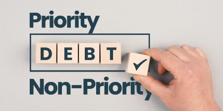 Priority-and-non-priority-debts-a-complete-guide-Feature Grey background with the text "Priority Debt and Non-Priority' with some wooden blocks displaying "Debt"