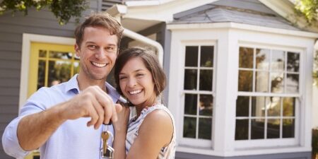 A couple standing outside of their new house, smiling with a set of keys