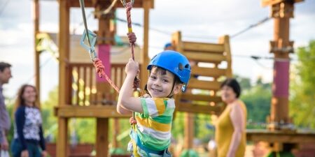 Cheap-or-Free-Activities-for-the-Kids-feature A child on a zipwire at a playground with family in the background