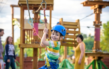 A child on a zipwire at a playground with family in the background