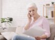 Middle-aged women sitting on her sofa with documents in one hand and speaking on the phone with the other.