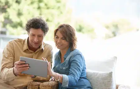 A couple sitting on the sofa, smiling and looking at an ipad.