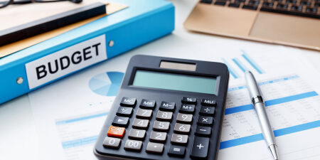 Tips-for-Budgeting-During-a-Recession-feature Image of a calculator, pen, laptop, reading glasses and a blue folder titled "budget."