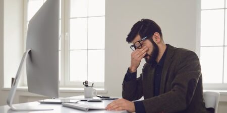 How-Debt-could-Affect-Your-Career-feature Man sat at a desk with his head in his hands.