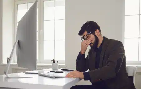 Man sat at a desk with his head in his hands.