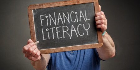 Improving-Financial-Literacy-feature An image of a man holding up a mini black board with the writing 'Financial Literacy'