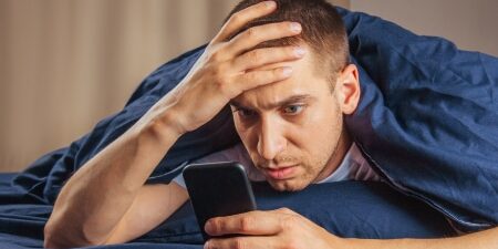 Does-Social-Media-Put-Your-Finances-Under-Pressure_-feature Image of a man lying down in bed on his mobile, looking concerned