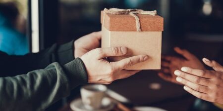 How-to-Manage-Gift-Giving-Expectations-While-in-Debt-feature An image of someone passing a wooden gift box to their friend.