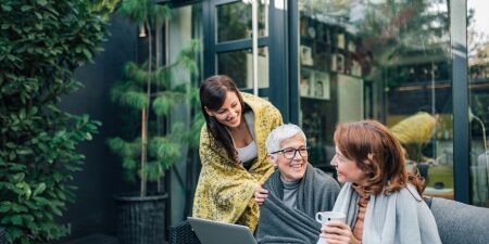 Image of a granddaughter, mother, and grandmother all sitting outside, smiling, with a laptop.