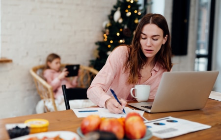 Image of a mother on her laptop writing her budget with her daughter in the background