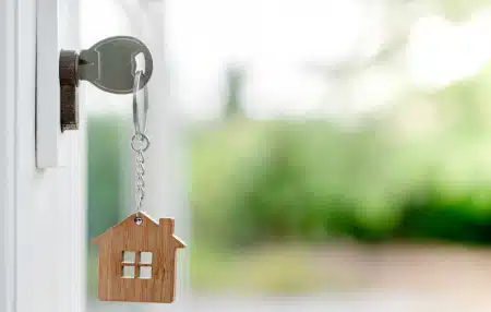 Image of a key in a front door with a wooden house keychain attached 