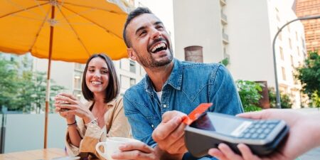 Breaking Bad… habits that cost_ How to break bad spending habits feature Image of a man and a woman smiling sitting outside of a restaurant paying for their coffee