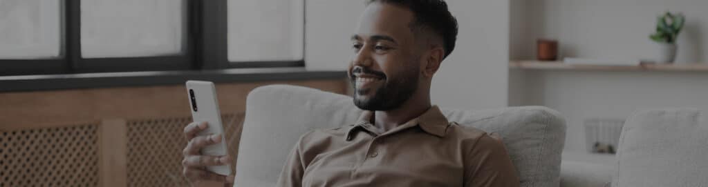 Image of a man sitting on his sofa smiling at his mobile phone