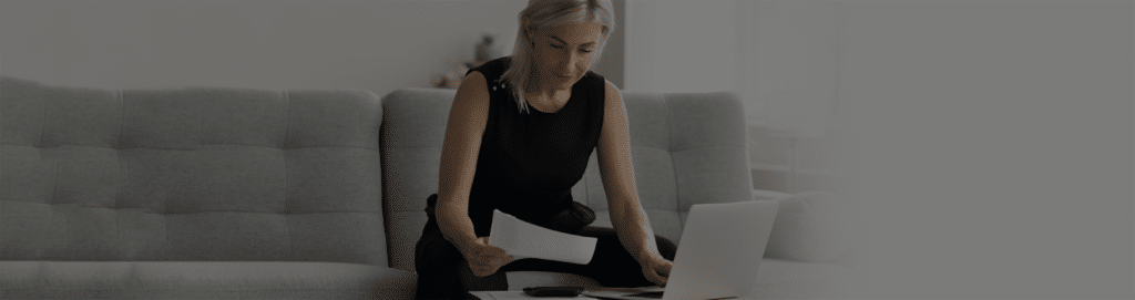 An image of a woman sitting on her sofa looking at papers and her laptop