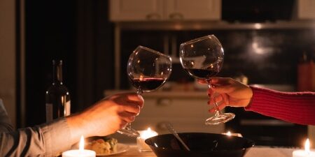 Image of a couple clinking their wine glasses together filled with red wine over a candlelit dinner