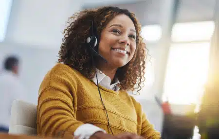 Image of a woman in a call centre, smiling whilst speaking to a client.