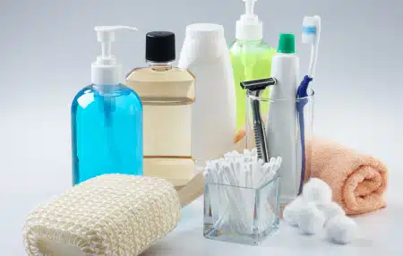 An image of toiletries including an orange flannel, blue bottle of liquid soap, mouthwash, shower gel, toothpaste, cotton ear buds, razors and toothpaste.