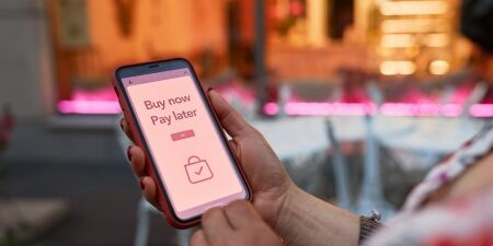 Rise of Buy Now Pay Later schemes feature Image of someone looking at their mobile with the words 'Buy Now Pay Later' displayed