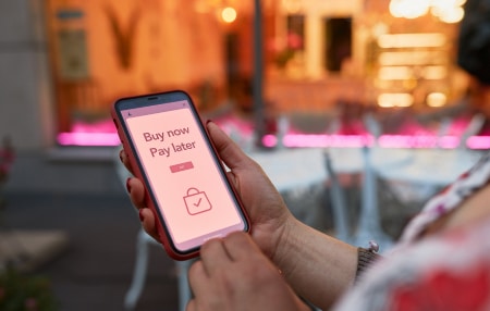 Image of someone looking at their mobile with the words 'Buy Now Pay Later' displayed 