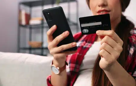 Image of a woman sitting on her sofa with her credit card in one hand and her phone in the other.