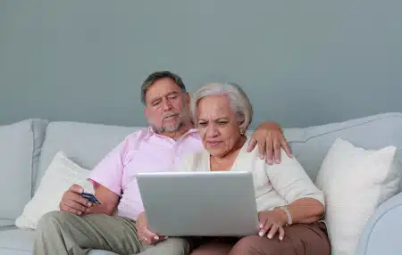 Image of a woman and a man sitting on the sofa looking at their laptop.