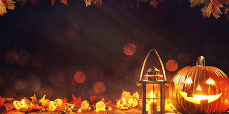 Halloween (feature) Image of a pumpkin lit up and a lantern on a dark background with autumn leaves