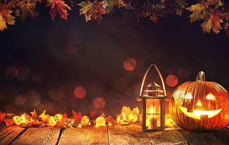 Image of a pumpkin lit up and a lantern on a dark background with autumn leaves 