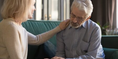 How To Talk To Your Partner About Debt feature Image of a woman comforting her husband on the sofa