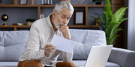 How to overcome debt depression (feature) Image of an older man sitting on his sofa reading a letter with his laptop.