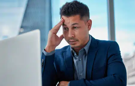 Image of a man with his head in his hands looking at his laptop screen