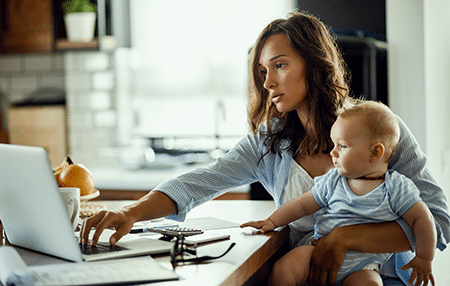 Imagine of a woman on her laptop whilst holding her baby