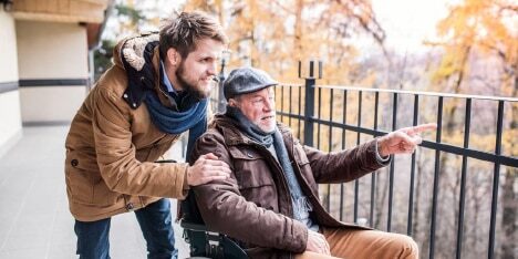 man-father A man using a wheelchair points at something over railings while his son and carer looks on.