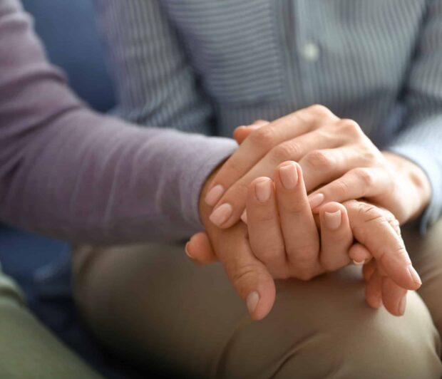Young daughter supporting elderly mother at home, closeup a close up of a young woman’s hand holding the hand of an elderly person.