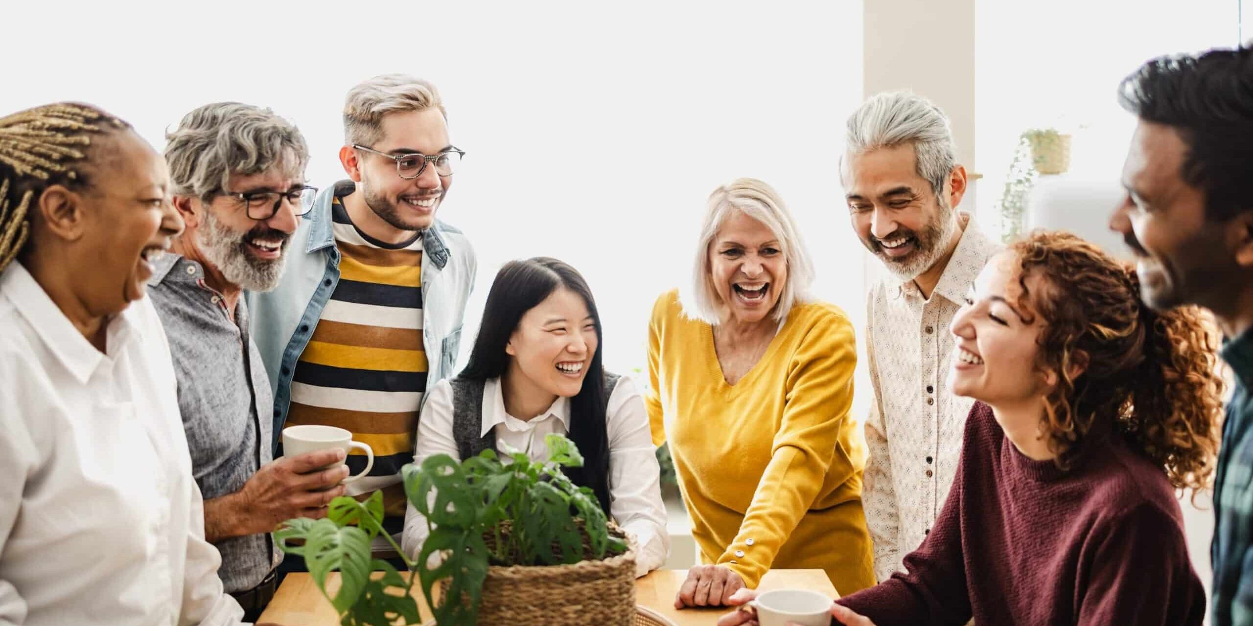 MP Group of diverse people smiling and talking around a table indoors.