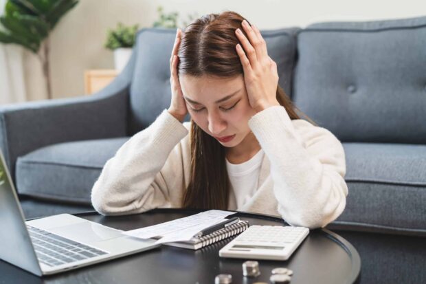 Stressed bankrupt financial crisis concept, Young adult in nervous after calculated loan expense and can not pay to bank. Worried woman looking at bills with a laptop and calculator on the table.