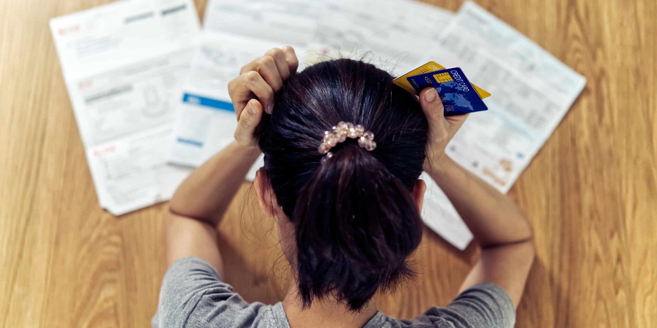 Top view of stressed young sitting Asian woman hands holding the Woman holding credit cards, stressed over bills on a table.