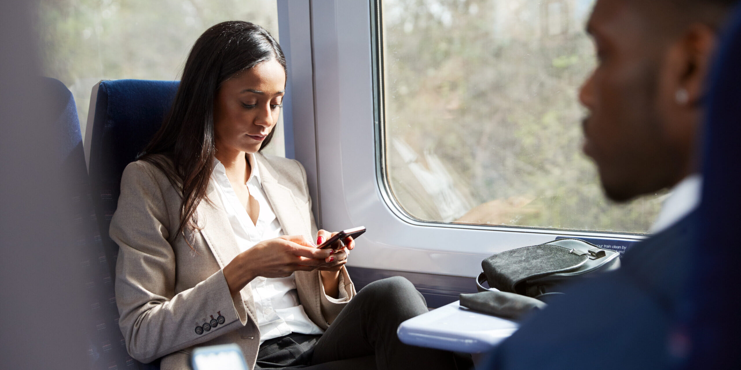 Business Passengers Sitting In Train Commuting To Work Looking At Mobile Phones