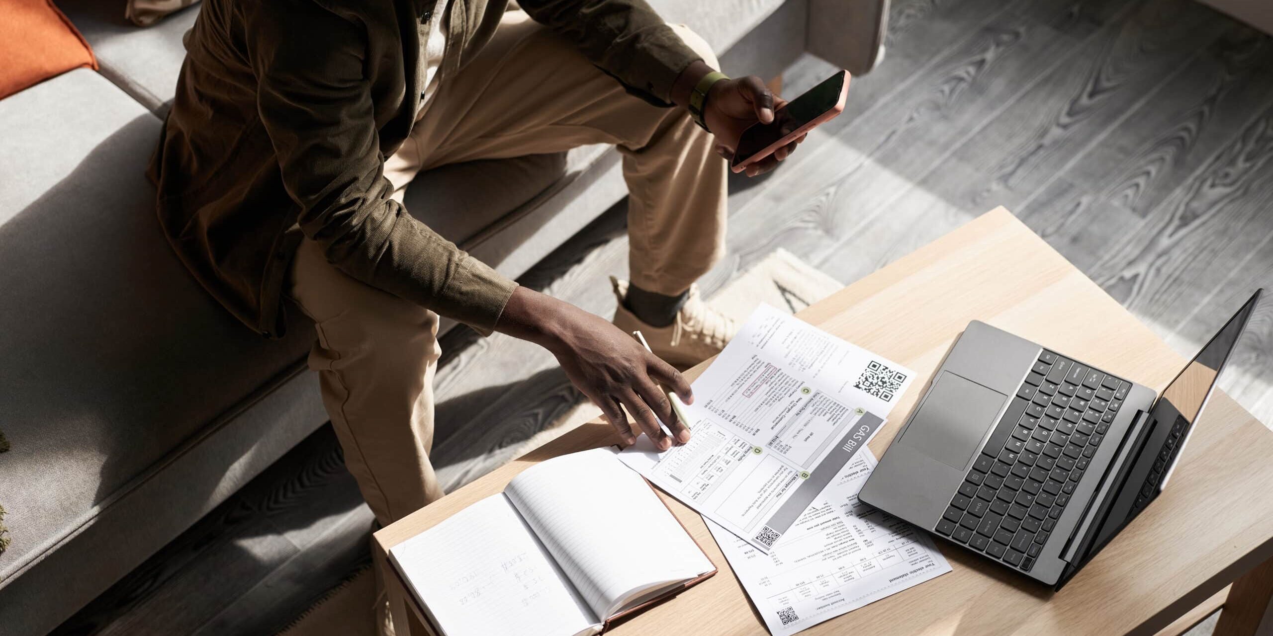 Black man doing taxes at home in sunlight with financial documents on table