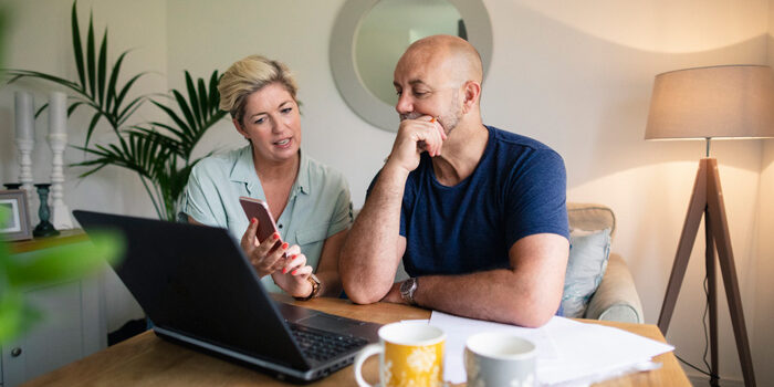 A front-view shot of a happy mature couple enjoying a hot drink while using their laptop, they are wearing casual clothing.