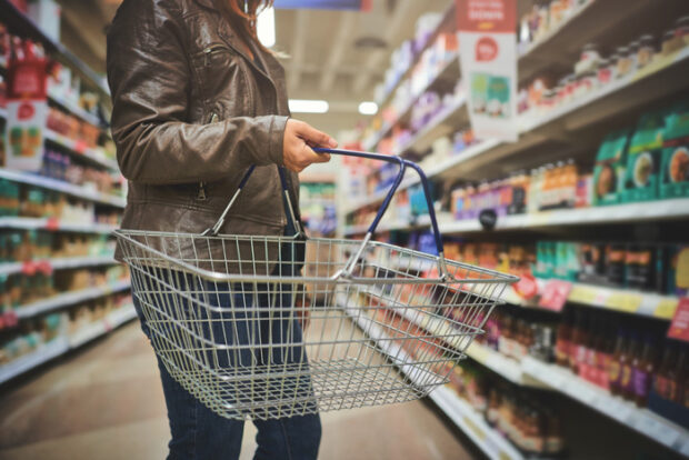 Cropped shot of a woman holding a basket while shopping at a grocery store